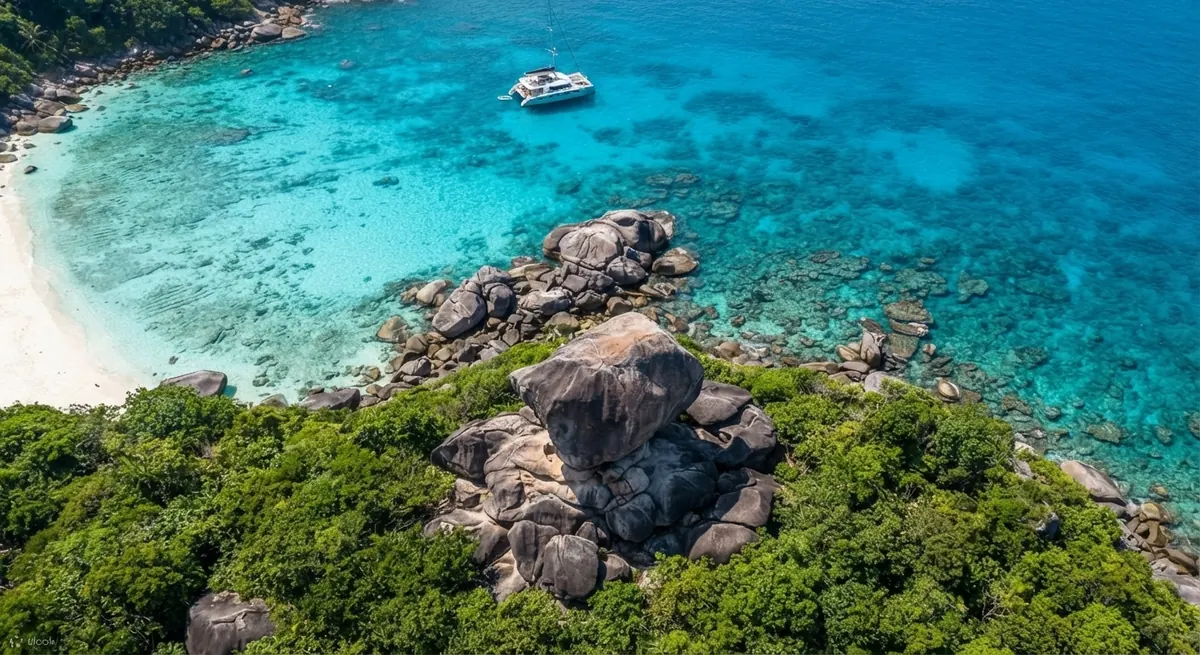 Aerial view of granite boulders, turquoise reef and an anchored catamaran