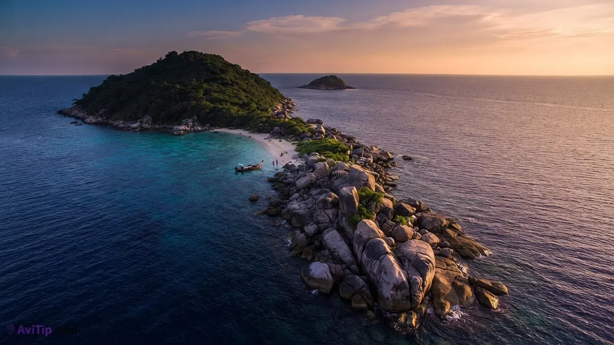 Aerial view of a forested island and a rocky spit in the Andaman Sea at dusk