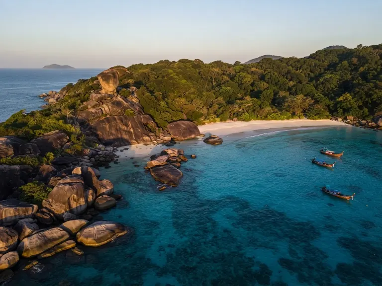 Aerial view of a sheltered Similan bay with boats moored over reef and granite headlands on both sides