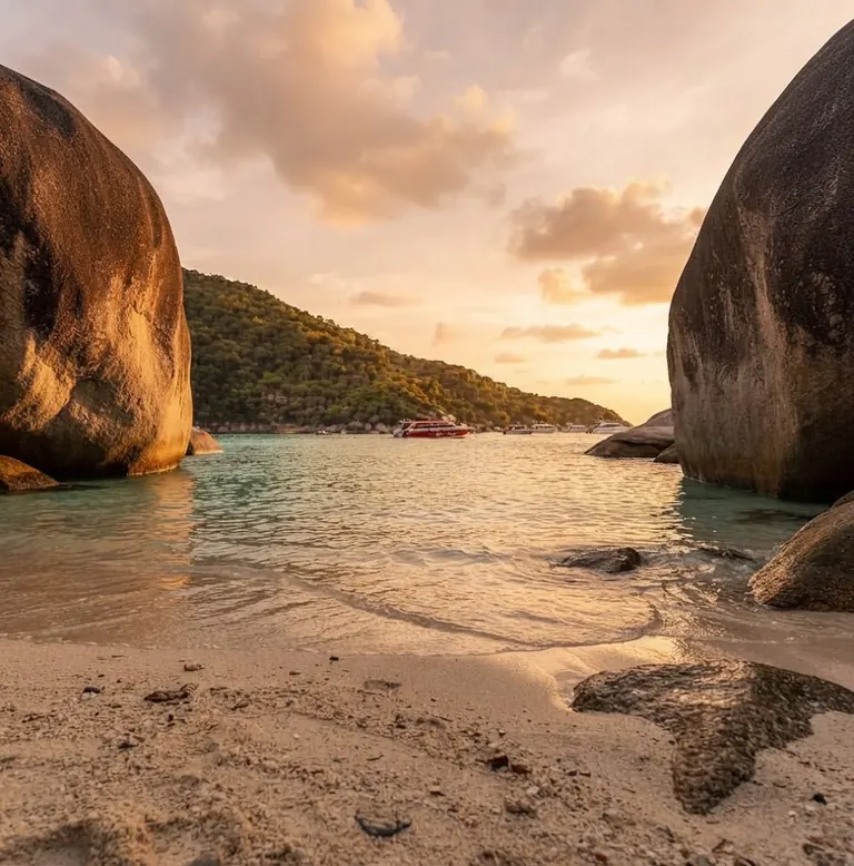 Beach framed by two granite boulders with a boat offshore at sunset