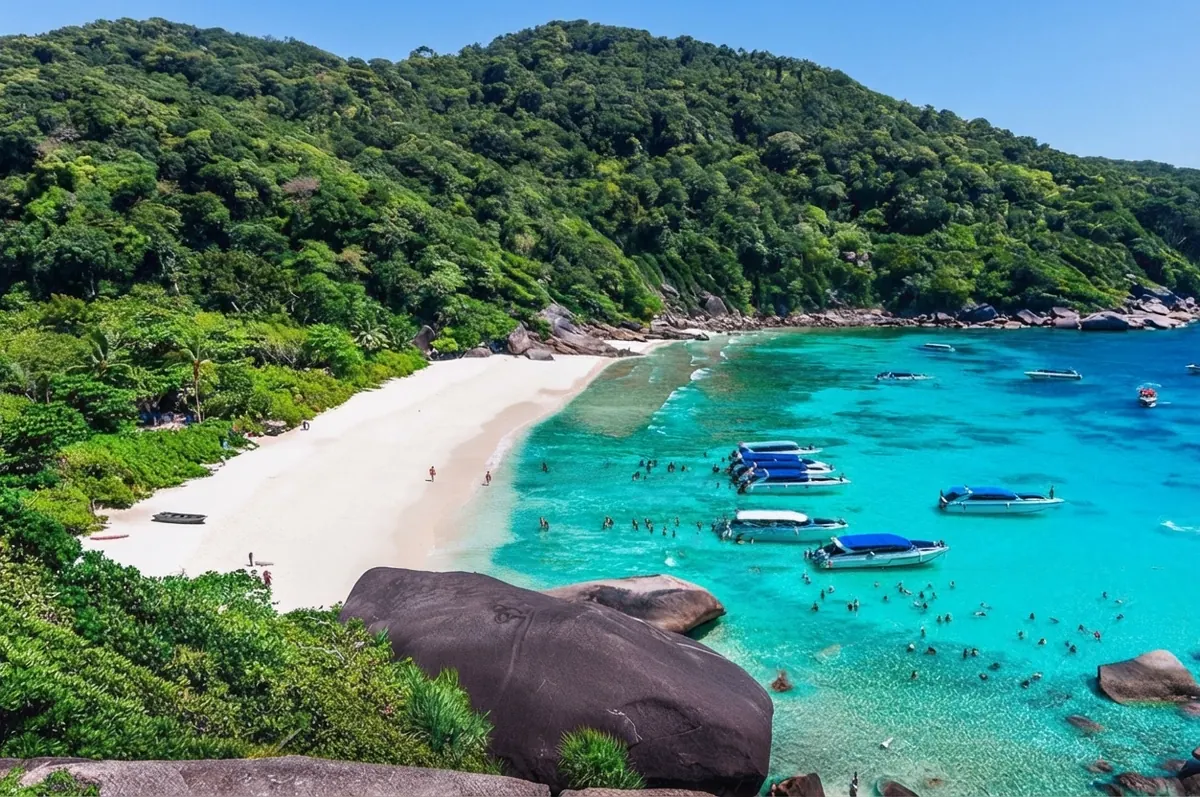 Speedboats and swimmers filling a turquoise bay below a white beach