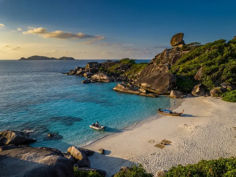 Donald Duck Bay at golden hour, a white beach curving below Sail Rock with longtail boats in the shallows