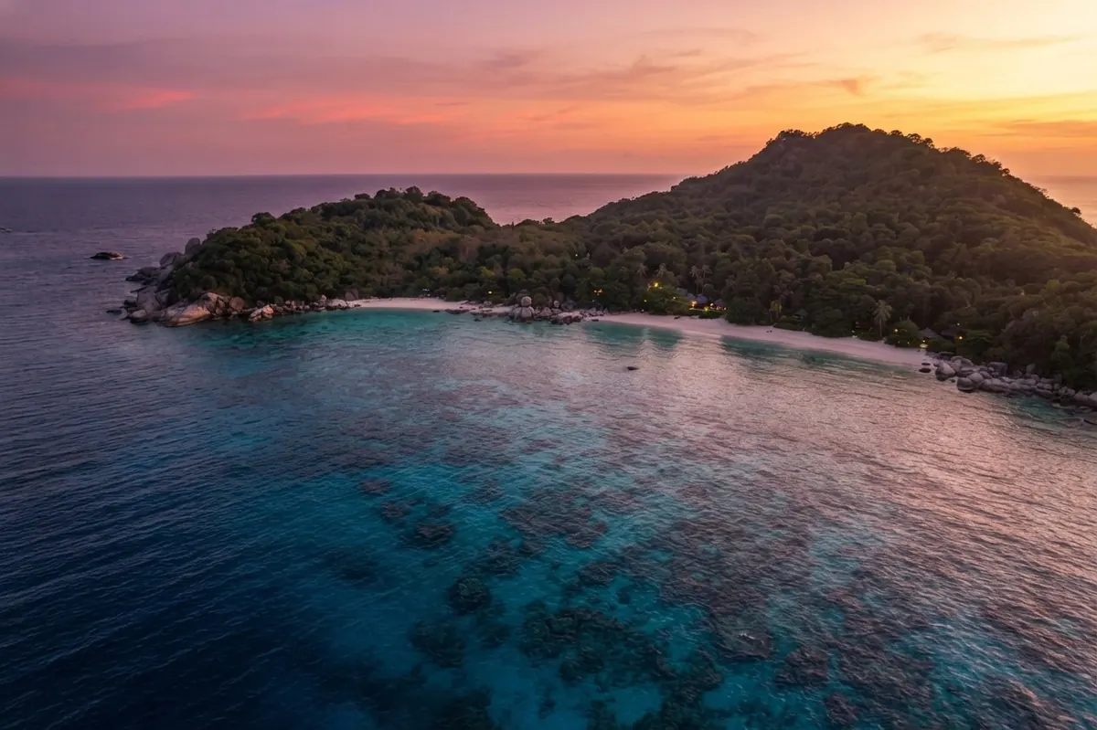 Forested island under a pink dusk sky over calm water