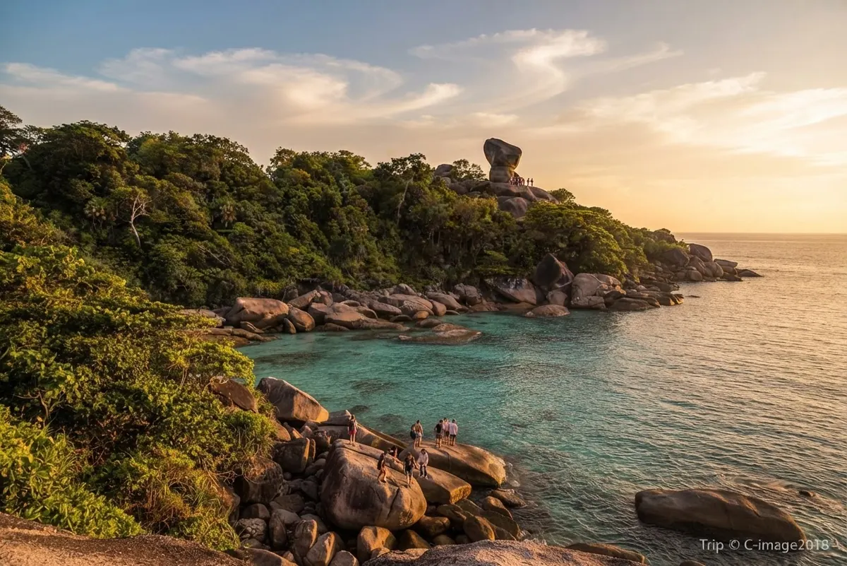 Forested island with a granite shoreline and Sail Rock on the skyline at sunset