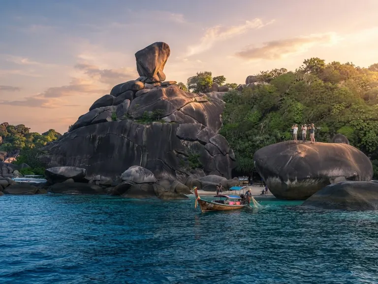 Longtail boat below Sail Rock at golden hour with visitors at the viewpoint