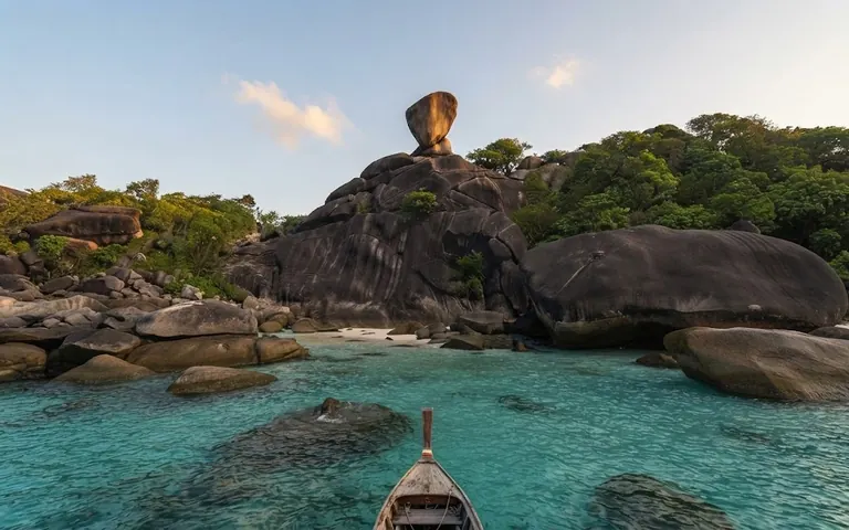 Bow of a longtail boat in a clear green lagoon below the granite boulders of Sail Rock