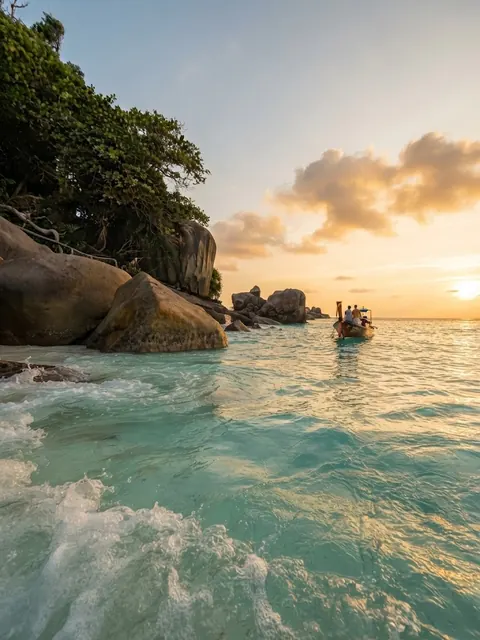 Small waves running up a Similan beach with a longtail boat offshore at sunset