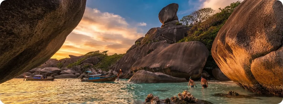 Wide panorama through two granite boulders towards Sail Rock and people wading in a lagoon