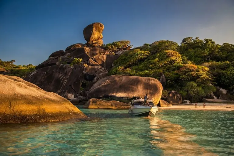 Sail Rock glowing at golden hour with a speedboat moored in the bay below