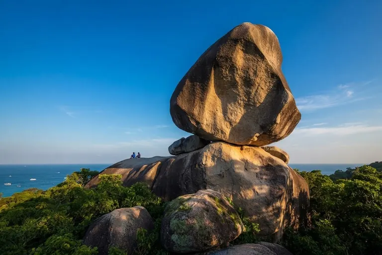 Visitors standing beside the balanced boulder of Sail Rock