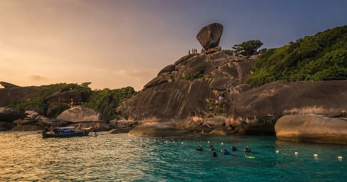 Snorkelers in the water below Sail Rock with longtail boats at anchor