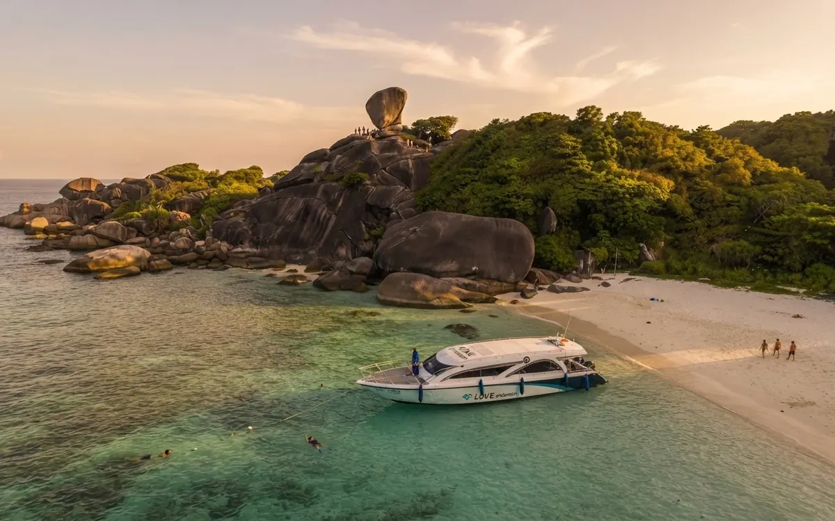 Speedboat moored off a white beach below Sail Rock at golden hour