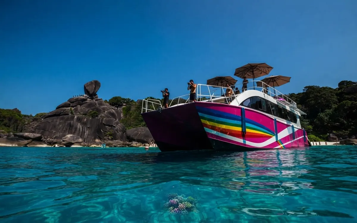 Colourful striped catamaran moored in turquoise water with Sail Rock behind