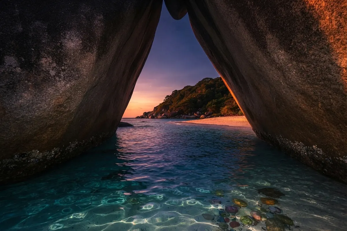 Sunset seen through an arch formed by two giant granite boulders over shallow water