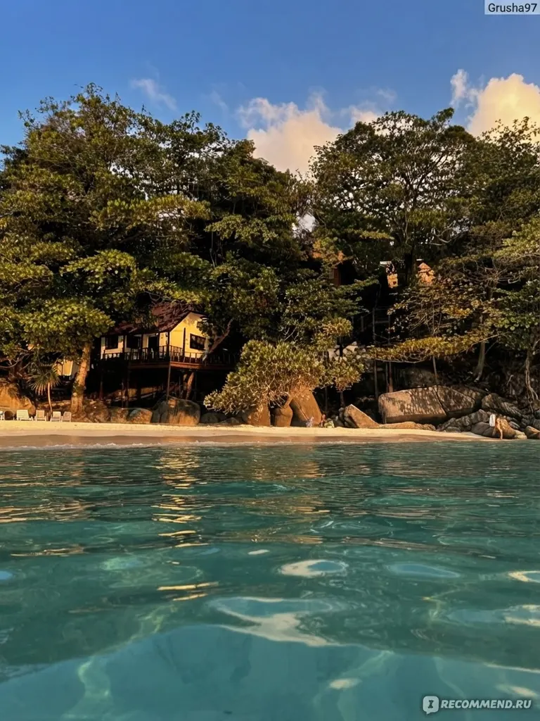 Wooden hut under tropical trees beside a calm, clear bay